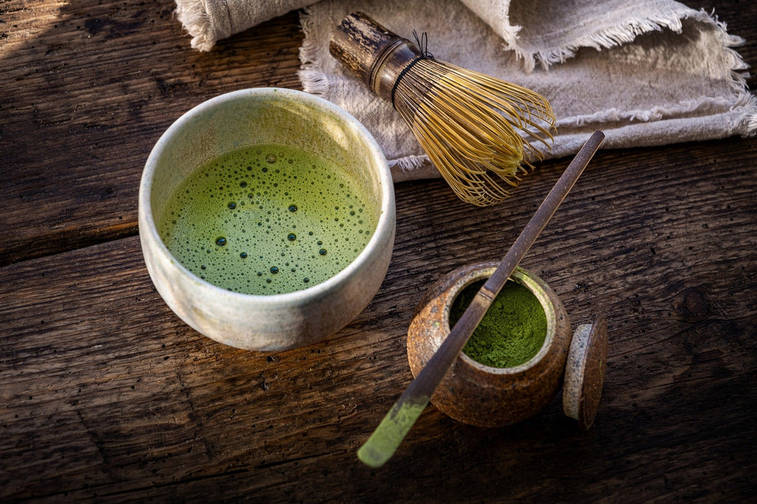 Vibrant green organic matcha tea powder being whisked into a frothy brew inside a traditional ceramic bowl.