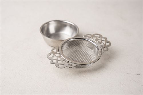 The Aurelian stainless steel tea infuser with decorative handles and a matching drip tray.